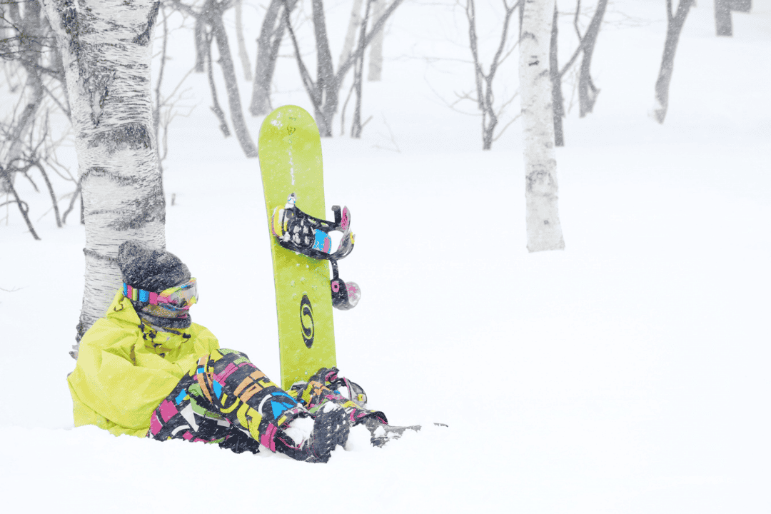 木の根元に座り込む女性スノーボーダー
